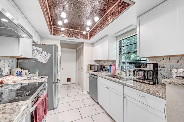 kitchen featuring stainless steel appliances, sink, decorative backsplash, white cabinetry, and a tray ceiling