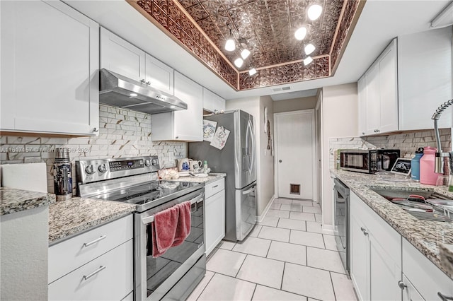 kitchen with white cabinets, backsplash, appliances with stainless steel finishes, and a tray ceiling