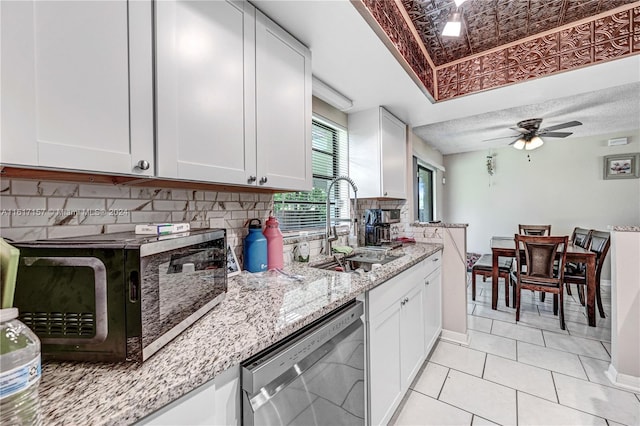 kitchen featuring stainless steel dishwasher, ceiling fan, white cabinets, light stone counters, and backsplash