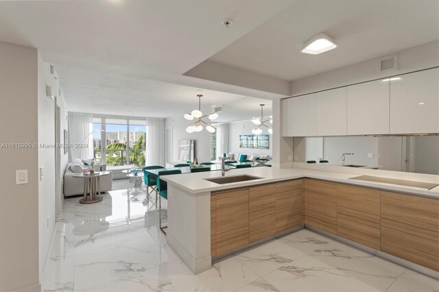 kitchen with hanging light fixtures, white cabinets, sink, an inviting chandelier, and kitchen peninsula