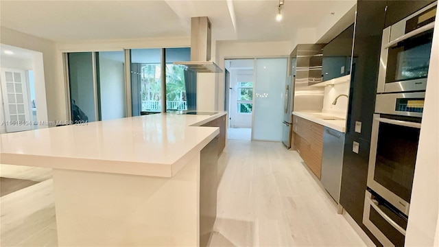 kitchen with sink, light wood-type flooring, a spacious island, stainless steel appliances, and ventilation hood