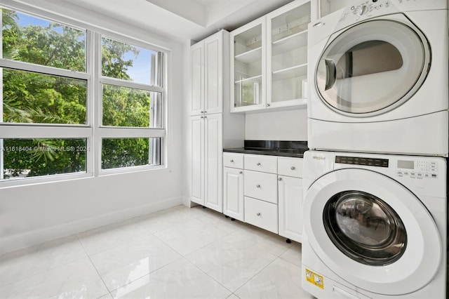 clothes washing area with cabinets and stacked washer and dryer