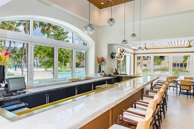 bar with a towering ceiling, light stone countertops, and decorative light fixtures