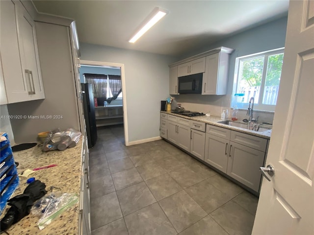 kitchen with sink, black appliances, tile patterned flooring, and light stone counters