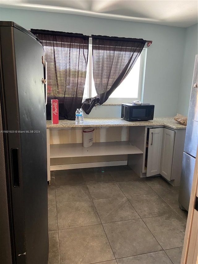 kitchen featuring tile patterned flooring, light stone countertops, built in desk, and stainless steel refrigerator