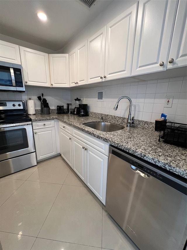 kitchen with light stone countertops, sink, light tile patterned floors, white cabinets, and appliances with stainless steel finishes