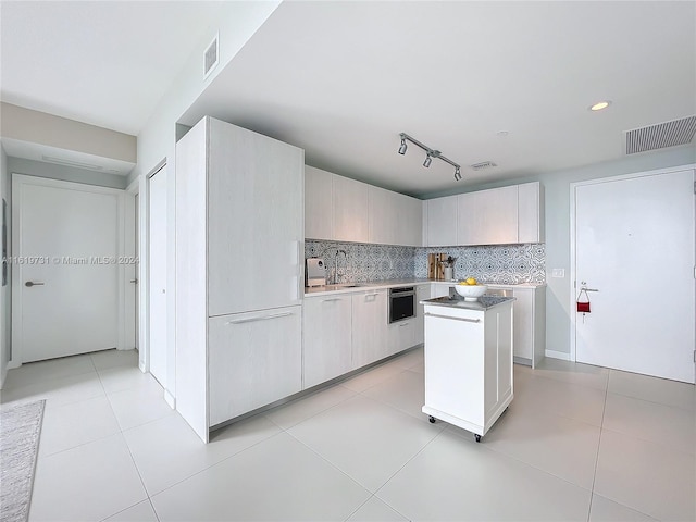 kitchen featuring stainless steel oven, light tile patterned floors, a center island, and tasteful backsplash