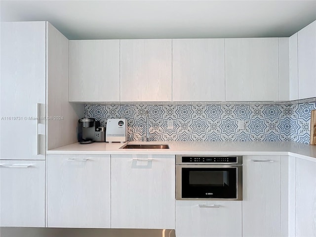 kitchen featuring white cabinets, backsplash, sink, and stainless steel oven