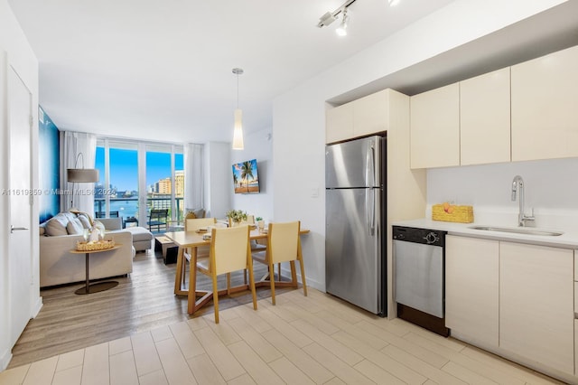 kitchen featuring track lighting, stainless steel appliances, sink, hanging light fixtures, and light hardwood / wood-style floors