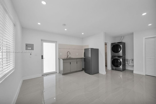 kitchen with light tile patterned floors, black refrigerator, stacked washer and clothes dryer, and sink