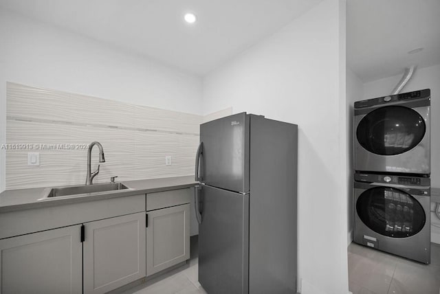 kitchen featuring black refrigerator, stacked washer and clothes dryer, light tile patterned floors, and gray cabinets