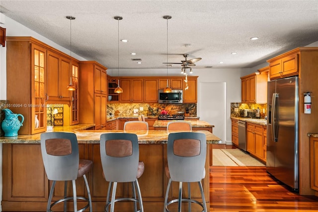 kitchen featuring kitchen peninsula, stainless steel appliances, ceiling fan, and hanging light fixtures