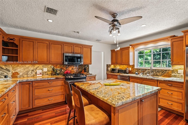 kitchen with stainless steel appliances, a kitchen island, ceiling fan, and dark hardwood / wood-style floors