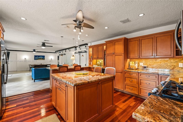 kitchen with light stone countertops, dark wood-type flooring, ceiling fan, and a center island