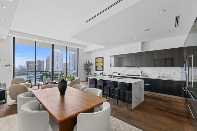 kitchen featuring a wall of windows, a kitchen island with sink, dark wood-type flooring, and sink