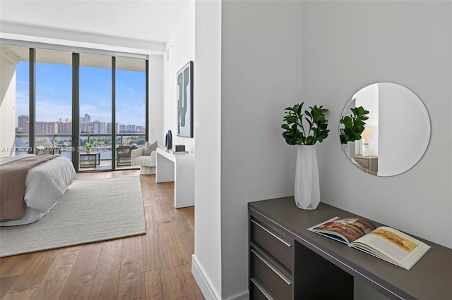 bedroom with a view of city, wood-type flooring, baseboards, and expansive windows