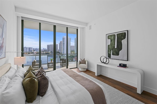 bedroom with a city view, wood finished floors, access to exterior, baseboards, and a wall of windows