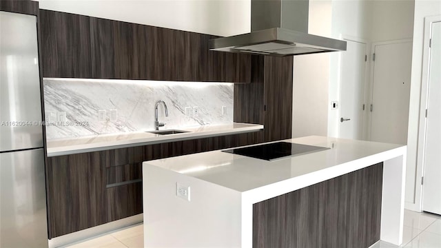 kitchen featuring stainless steel refrigerator, backsplash, island range hood, a kitchen island, and black electric cooktop