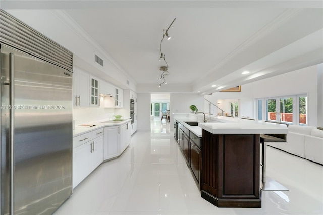 kitchen featuring tasteful backsplash, a center island with sink, white cabinetry, stainless steel appliances, and dark brown cabinets