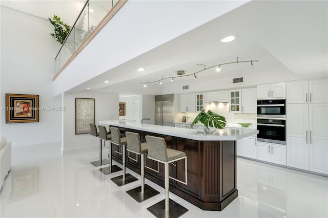 kitchen featuring white cabinetry, stainless steel appliances, decorative backsplash, a spacious island, and a breakfast bar