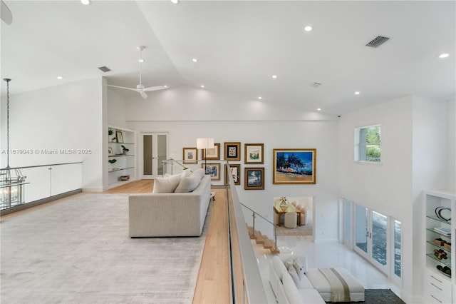 living room featuring high vaulted ceiling, built in shelves, light hardwood / wood-style flooring, and ceiling fan