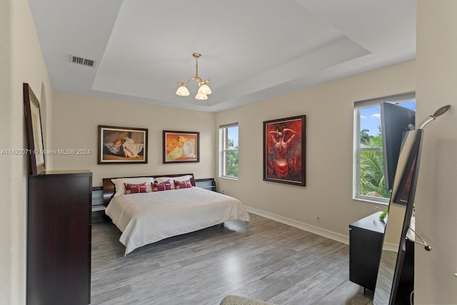 bedroom with wood-type flooring, a raised ceiling, and a notable chandelier