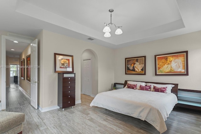 bedroom with a notable chandelier, a raised ceiling, and hardwood / wood-style floors