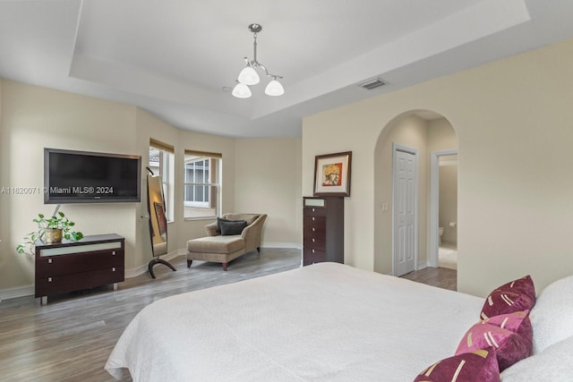 bedroom with an inviting chandelier, a tray ceiling, hardwood / wood-style flooring, and a closet