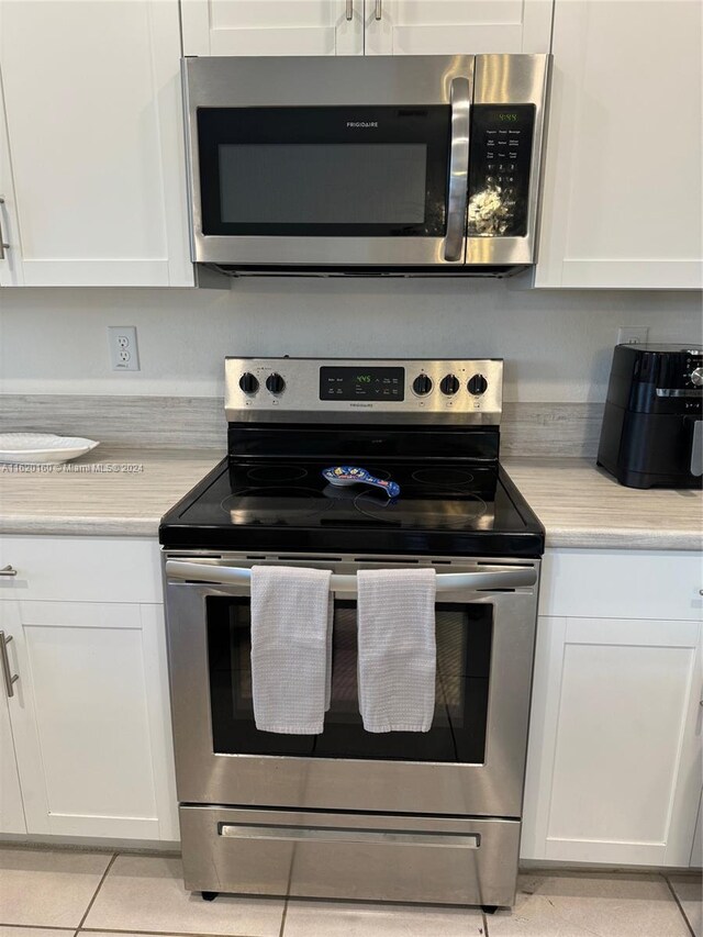 kitchen featuring appliances with stainless steel finishes, light tile patterned floors, and white cabinetry