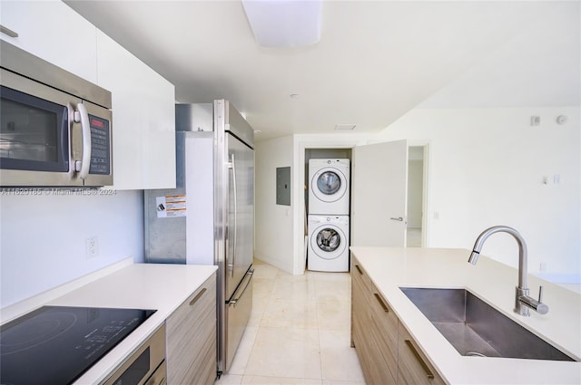 kitchen featuring sink, electric panel, electric stovetop, light tile patterned floors, and stacked washer / drying machine