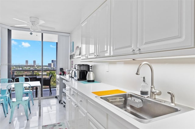 kitchen featuring sink, light tile patterned floors, ceiling fan, white cabinetry, and expansive windows