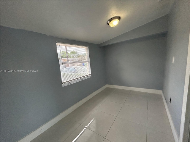 tiled empty room featuring vaulted ceiling