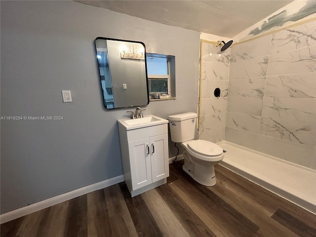 bathroom with wood-type flooring, vanity, a tile shower, and toilet