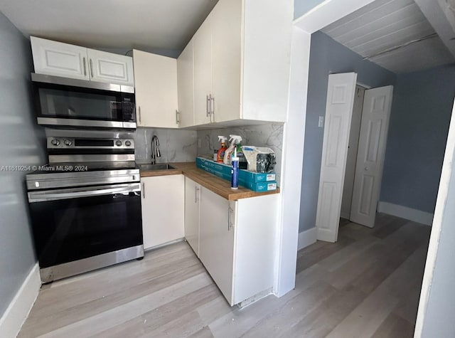 kitchen with sink, light wood-type flooring, appliances with stainless steel finishes, tasteful backsplash, and white cabinetry