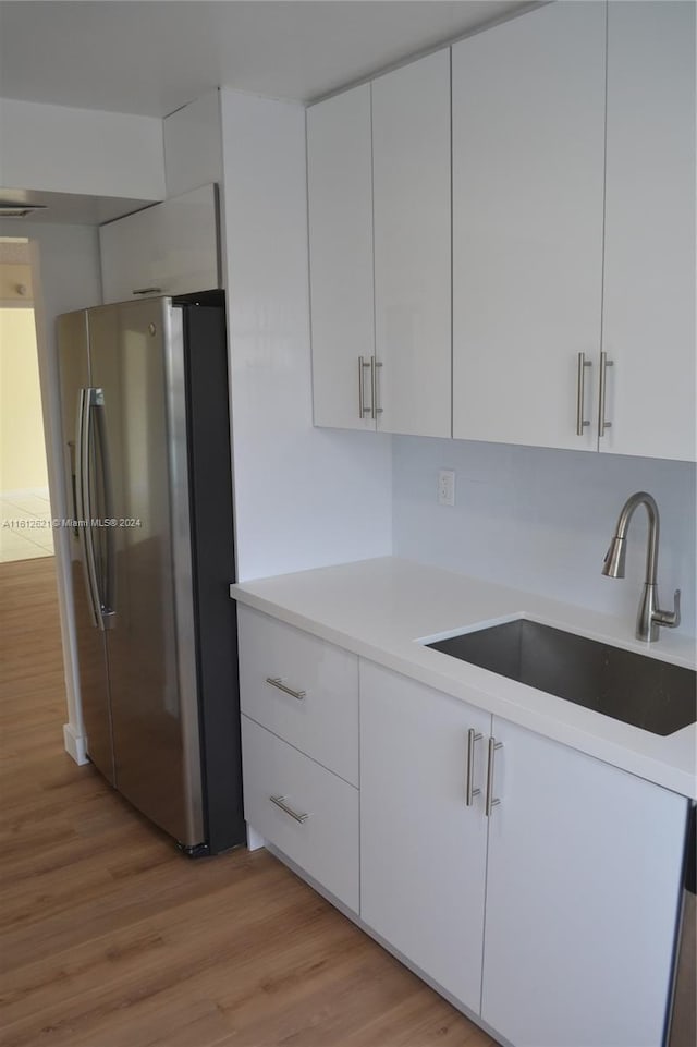 kitchen featuring sink, stainless steel fridge, white cabinets, and light wood-type flooring