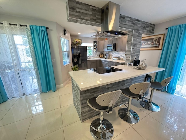 kitchen featuring tasteful backsplash, light tile patterned floors, island range hood, black appliances, and kitchen peninsula