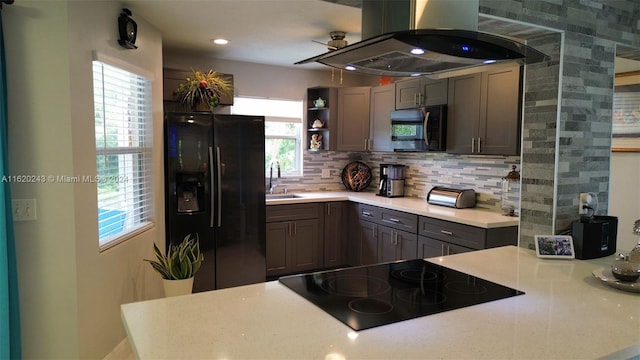 kitchen featuring decorative backsplash, island range hood, black appliances, and a healthy amount of sunlight