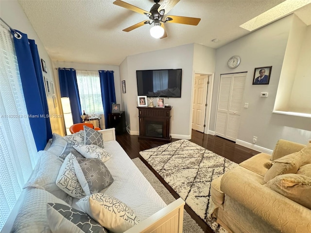 living room featuring ceiling fan, lofted ceiling with skylight, dark hardwood / wood-style flooring, and a textured ceiling