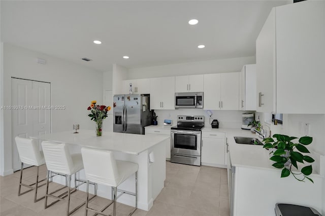 kitchen featuring stainless steel appliances, a kitchen island, a sink, white cabinets, and a kitchen bar