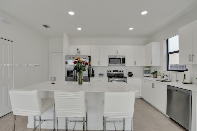 kitchen with stainless steel appliances, light countertops, white cabinets, a sink, and a kitchen island