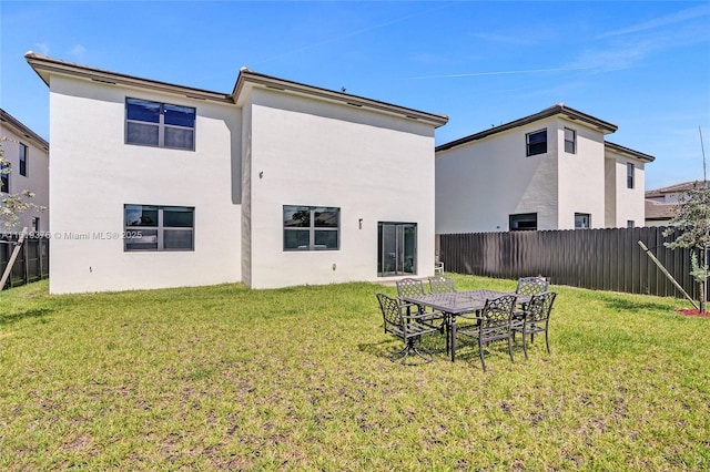 back of house featuring fence private yard, stucco siding, and a yard