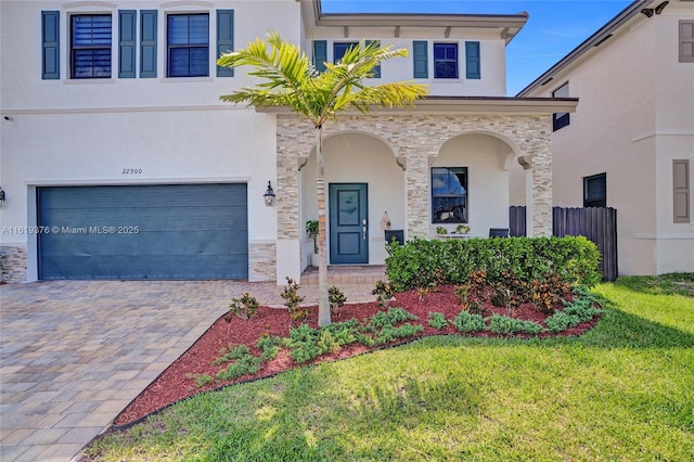 view of front of property featuring a garage, stone siding, decorative driveway, and stucco siding