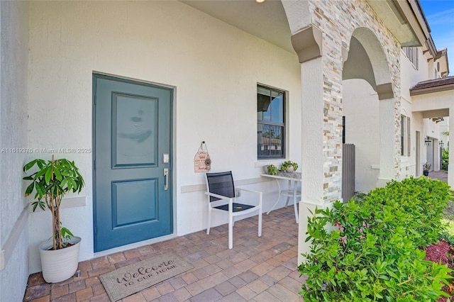 doorway to property with stone siding, a porch, and stucco siding