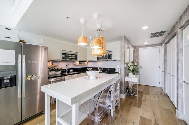 kitchen featuring stainless steel appliances, pendant lighting, sink, a kitchen island, and light hardwood / wood-style flooring