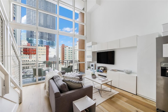 living room with expansive windows, light wood-type flooring, a healthy amount of sunlight, and a towering ceiling