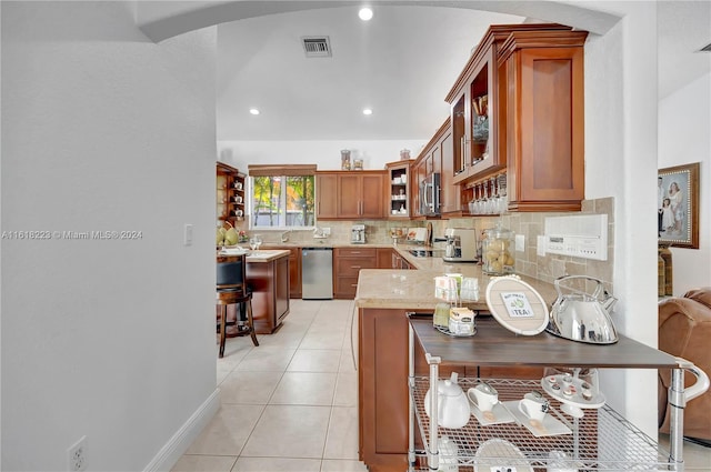 kitchen featuring light stone countertops, a kitchen breakfast bar, kitchen peninsula, decorative backsplash, and light tile patterned floors