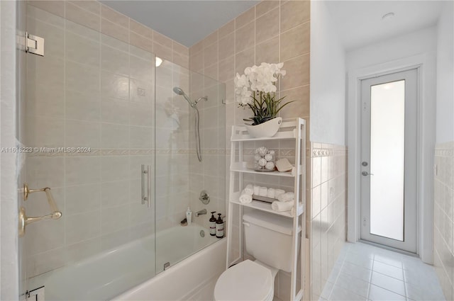 bathroom featuring tile patterned floors, a healthy amount of sunlight, shower / bath combination with glass door, tile walls, and toilet