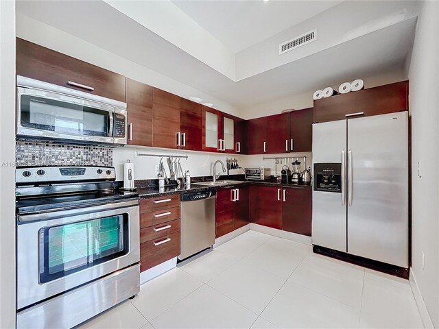 kitchen with stainless steel appliances, decorative backsplash, sink, dark stone countertops, and light tile patterned floors