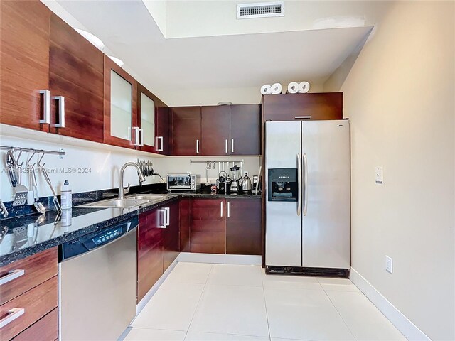 kitchen featuring sink, dark stone countertops, light tile patterned floors, and stainless steel appliances