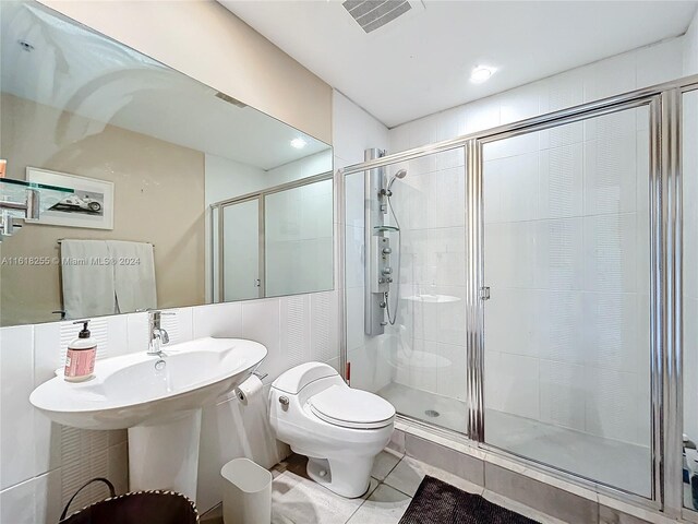 bathroom featuring tile patterned floors, a shower with shower door, toilet, and tile walls